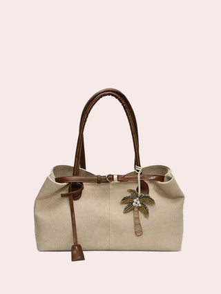 A beige textured leather handbag with brown leather handles and trim, featuring a hanging palm tree charm, set against a light beige background with the brand name 'FEISTURE' printed in black at the top.